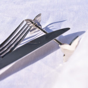 Knife resting on a knife rest , porte couteau with butterlfies on each end. Pictured on a white tablecloth with a fork