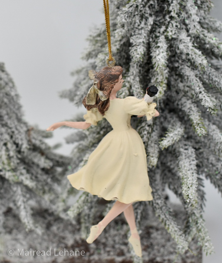 Ballerina with hair tied back with a bow,in a pale cream dress, with ballet shoes and carrying a nutcracker doll in her arms ac