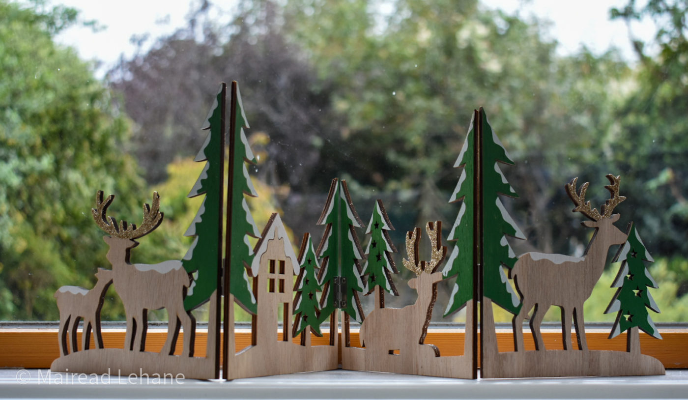 festive wooden panel decoration with cut out reindeer , hut and trees