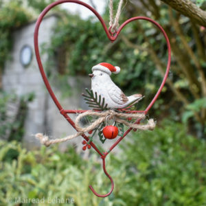 red heart shaped bird feeder with small white bird wearing a santa hat