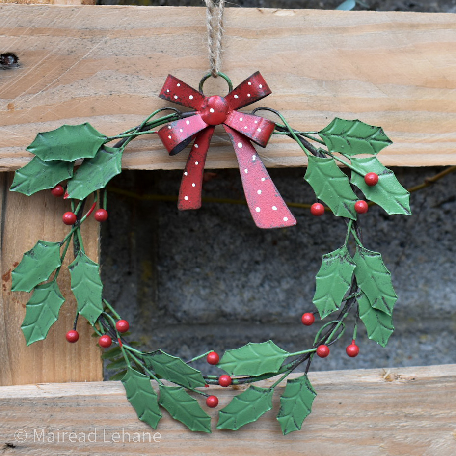 metal wreath with green leaves, red berries and red and wiite bow with a wooden background