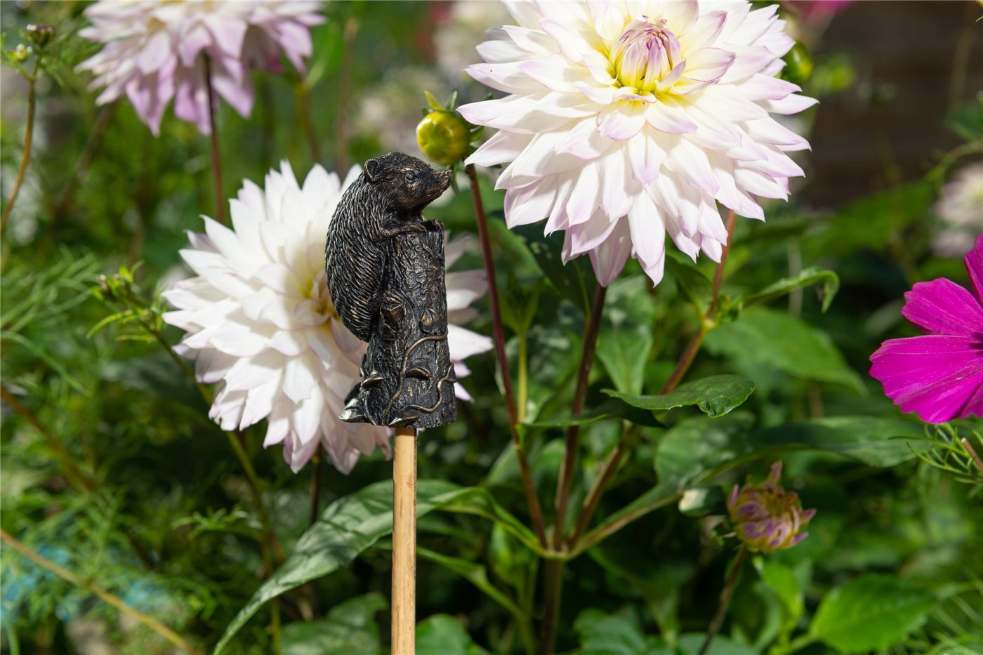hedgehog topper on a stake in the garden surrounded by flowers
